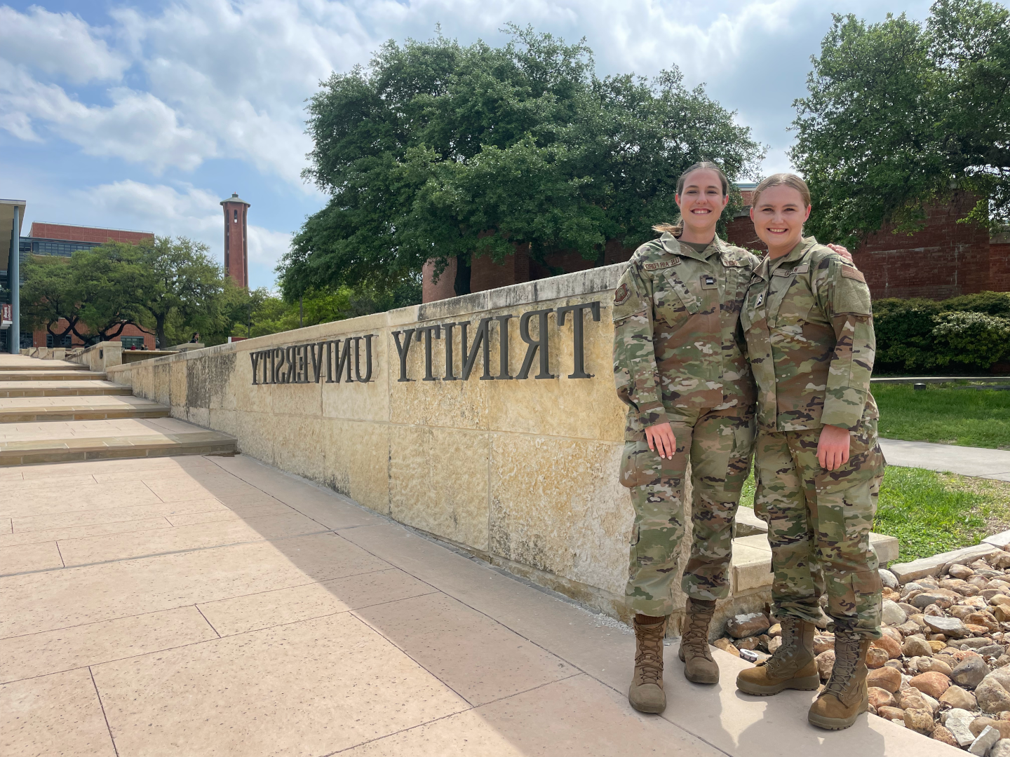 Two Trinity students in Army camouflage uniforms standing in front of Trinity University sign. 